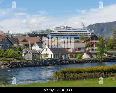 Un villaggio lungo il fiume con una grande nave da crociera sullo sfondo, circondato da montagne sotto un cielo limpido, Eidfjoerd, Norvegia, Scandinavia Foto Stock