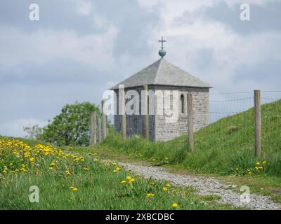 Chiesa in pietra con recinzione a picchetto su un sentiero verde, circondata da fiori gialli e cielo nuvoloso, haugesund, norvegia, scandinavia Foto Stock