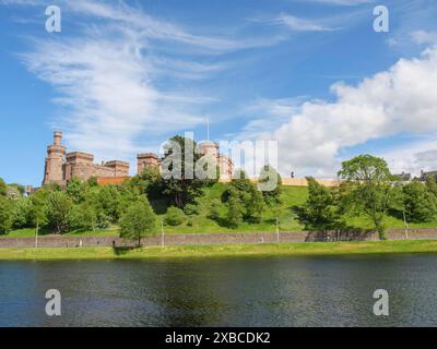 Un castello su una collina verde circondato da alberi con un fiume in primo piano e un cielo blu, inverness, scozia, Gran Bretagna Foto Stock