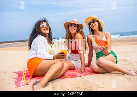 Amici che si godono l'estate in spiaggia in vacanza, seduti sulla sabbia Foto Stock