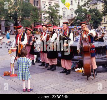 Una bambina ascolta una banda musicale di uomini anziani vestiti con costumi nazionali polacchi in una piazza di Cracovia, Polonia, Europa. Diapositiva 6x6 scansionata, Europa Foto Stock