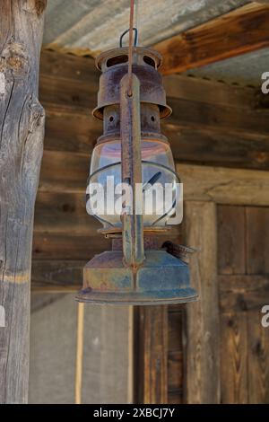 Lampada dei minatori rugginiti appesa al travetto su portico rustico in legno Foto Stock