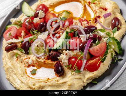 Hummus greco carico di cetrioli freschi, olive, pomodori, formaggio feta, cipolle rosse e timo sul piatto, primo piano, vista dall'angolo olandese Foto Stock