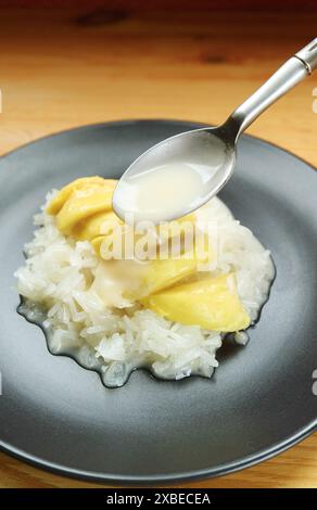 Cucchiaio che aggiunge latte di cocco al delizioso riso Thai Sticky con Durian chiamato Kao Niaow Turian Foto Stock