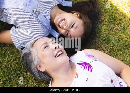 Nonna asiatica e nipote birazziale sdraiata sull'erba, sorridente e divertendosi Foto Stock