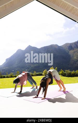 Nonna asiatica e nipote birazziale che fanno yoga insieme nella giornata di sole. Si trovano su un patio con una vista panoramica delle montagne sullo sfondo, godendosi Foto Stock