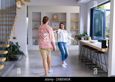 Giovani coppie diverse si divertono insieme a casa. Sono in uno spazio soggiorno moderno e luminoso, con grandi finestre e un decor elegante, inalterato Foto Stock