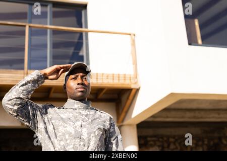 Giovane soldato afroamericano in uniforme militare che saluta fuori da un edificio moderno Foto Stock