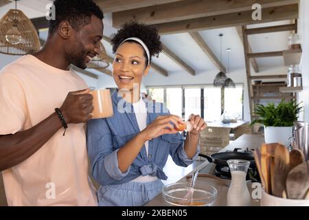 Una coppia giovane e variegata che prepara la colazione in una cucina moderna. sorridere e fare uova, inalterate Foto Stock