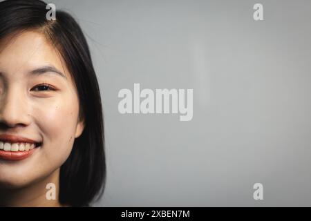 Giovane donna asiatica sorridente calorosamente, copia spazio. In posizione professionale con uno sfondo grigio semplice, inalterato Foto Stock