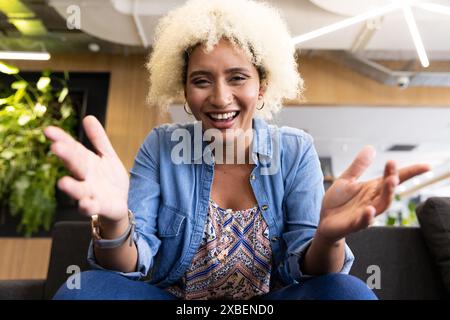 Giovane donna birazziale che sorride in videochiamata in ufficio Foto Stock