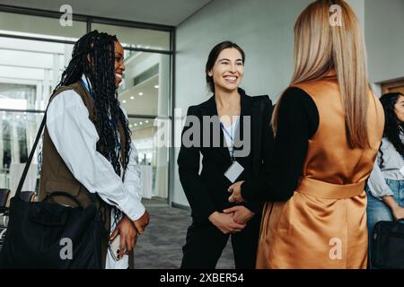 Tre donne d'affari che fanno networking, sorridono e conversano in un ambiente professionale. Ideale per le aziende, il networking e i temi professionali. Foto Stock