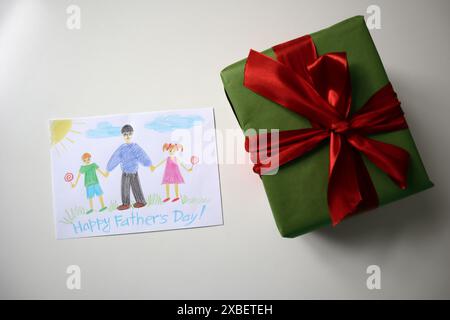 Festa del papà foto di una cartolina disegnata da un bambino. Un regalo di colore verde con un fiocco rosso. Sfondo bianco. La cartolina mostra un padre che cammina con ciao Foto Stock