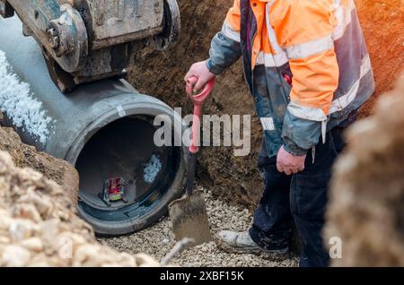 Lavoratori a terra che posano nuovi tubi in calcestruzzo durante i lavori di drenaggio profondo del nuovo progetto di edilizia abitativa Foto Stock