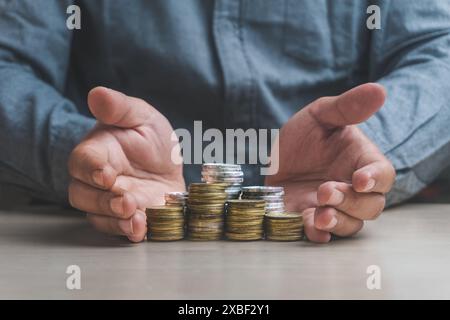 L'uomo d'affari protegge a mano un mucchio di monete simbolo monetario per le banche finanziarie aumenta il tasso di interesse o il dividendo degli investimenti ipotecari dalla crescita delle imprese Foto Stock