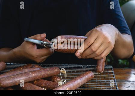 Un uomo sta tagliando una salsiccia che utilizza involucro di collagene, sarà cucinato utilizzando la tecnica di affumicatura Foto Stock
