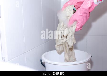 donna che utilizza guanti di gomma lavando a mano camicia bianca sporca con detergente e sbiancante in un cestello Foto Stock