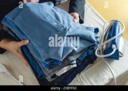 donna che raccoglie una pila di vestiti che hanno finito di stirare e piegare, finito i lavori domestici Foto Stock