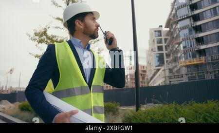 Appaltatore caucasico ingegnere civile addetto alla manutenzione elettrica che tiene il piano piano piano di progetto maschio che guarda all'uomo costruttore edile di edifici urbani Foto Stock