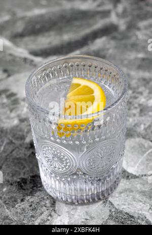 Una bevanda fresca e rinfrescante servita in un vetro di cristallo ornato con una fetta di limone, posta su una superficie di marmo. Foto Stock