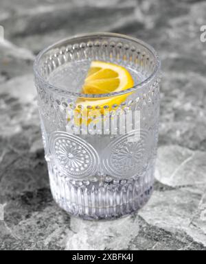 Una bevanda fresca e rinfrescante servita in un vetro di cristallo ornato con una fetta di limone, posta su una superficie di marmo. Foto Stock