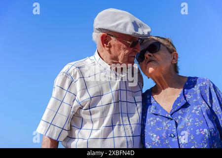 Coppia anziana che si baciano con un cielo blu. La scena è affettuosa e familiare Foto Stock