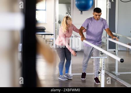 Un uomo birazziale sottoposto ad esercizi di riabilitazione con fisioterapista femminile. Sono in un moderno centro di riabilitazione con varie attrezzature e. Foto Stock