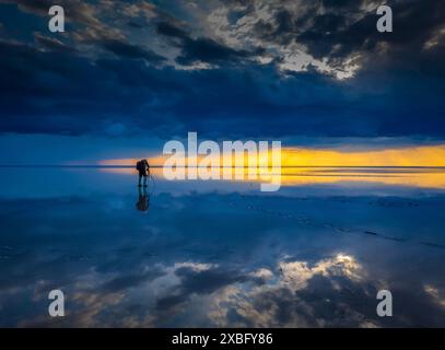 Un fotografo solitario scatta foto di un tramonto mozzafiato che si riflette su una calma salina, catturando la bellezza e la tranquillità della natura. Foto Stock