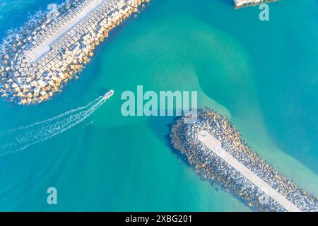 vista dall'alto di una barca da pesca che entra in un porto protetto da frangiflutti, immagine di un drone Foto Stock