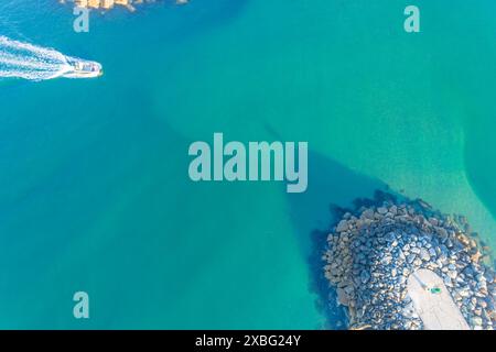 vista aerea direttamente sopra una barca da pesca che entra in un porto protetto da frangiflutti, immagine di un drone Foto Stock