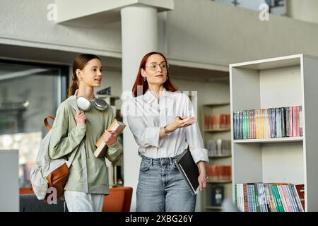 Una donna rossa insegna a una ragazza adolescente in una biblioteca, ingrossata di libri Foto Stock