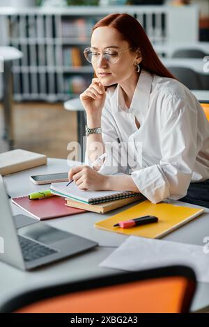 Una tutor dai capelli rossi si siede a una scrivania e insegna online con un portatile dopo una lezione scolastica. Foto Stock