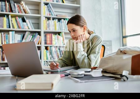 L'adolescenza si assorbe nel portatile mentre completa il lavoro scolastico in un ambiente sereno in biblioteca. Foto Stock