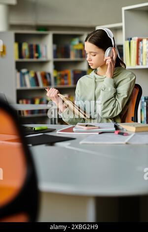 Una ragazza adolescente che indossa le cuffie si concentra sul suo notebook mentre è seduta a una scrivania in una biblioteca. Foto Stock