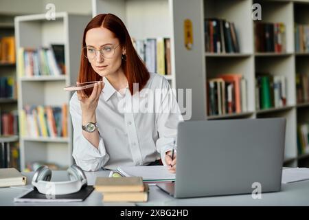 Una tutor donna rossa siede a una scrivania e si concentra sull'insegnamento di una lezione online usando un portatile, dopo la scuola. Foto Stock