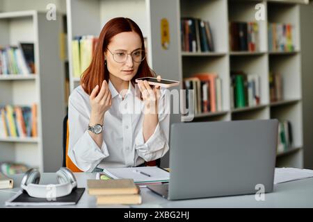 Una tutor rossa insegna online, seduto a una scrivania con un portatile davanti a lei. Foto Stock