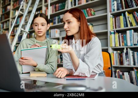 adolescente e tutor con i capelli rossi, partecipa a una moderna sessione educativa in una biblioteca, concentrandosi sullo schermo di un notebook. Foto Stock