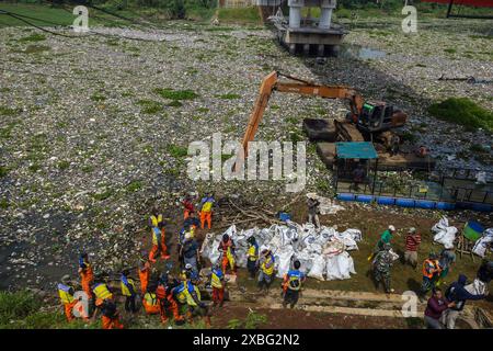 Gli ufficiali che utilizzano un escavatore anfibio ripuliscono i rifiuti di plastica che si sono depositati nel fiume Citarum a Batujajar, West Bandung Regency, West Java, Indonesia il 12 giugno 2024. Sulla base del servizio per l’ambiente e l’igiene della provincia occidentale, i registri dei rifiuti bloccati nel flusso fluviale da venerdì 7 giugno 2024 nella zona del fiume Citarum Batujajar, che è lungo 3 chilometri e largo 60 metri, si stima che il volume dei rifiuti di plastica potrebbe raggiungere oltre 100 tonnellate. (Foto di Dimas Rachmatsyah/Sipa USA) Foto Stock