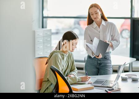 Una tutor rossa e una ragazza adolescente si dedicano a lezioni dopo la scuola alla scrivania, utilizzando un notebook per l'istruzione moderna. Foto Stock