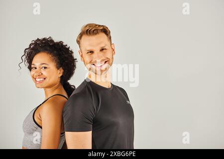 La giovane coppia sportiva interrazziale in vestibilità attiva si mette in posa insieme su uno sfondo grigio da studio. Foto Stock