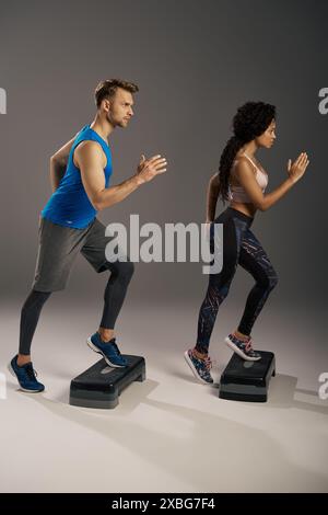 Una giovane coppia multiculturale con abbigliamento attivo che corre energicamente sugli stepper in un ambiente da studio. Foto Stock