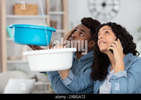 la coppia raccoglie l'acqua che fuoriesce dal soffitto e chiama l'idraulico Foto Stock