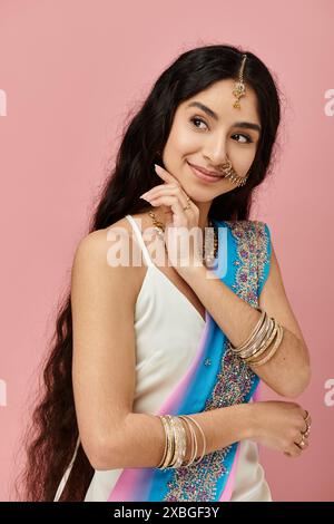 Giovane donna indiana in sari blu e bianco posa graziosamente su sfondo rosa. Foto Stock