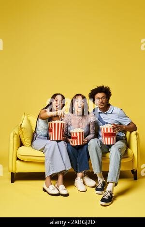 Tre giovani amici multiculturali si siedono su un divano, vestiti elegantemente, tenendo in mano secchi di popcorn. Foto Stock