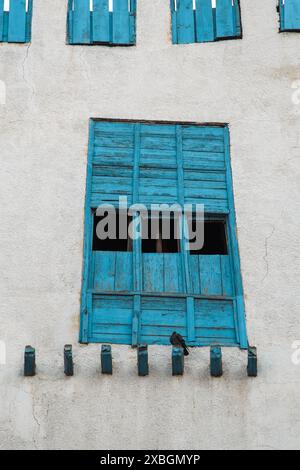 Jeddah, Arabia Saudita - 12 dicembre 2022: Una finestra blu intemprata nello storico quartiere di al-Balad, con un uccello solitario arroccato sotto, sho Foto Stock