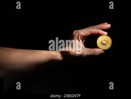 kiwi dorati a fette a mano su sfondo nero Foto Stock