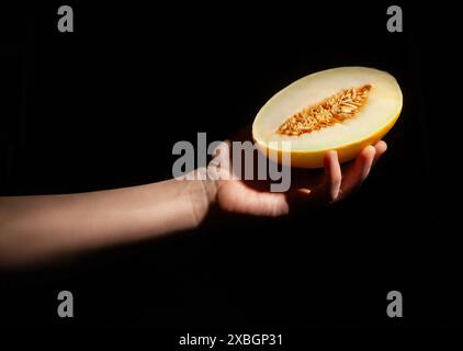 melone a fette in mano su sfondo nero Foto Stock