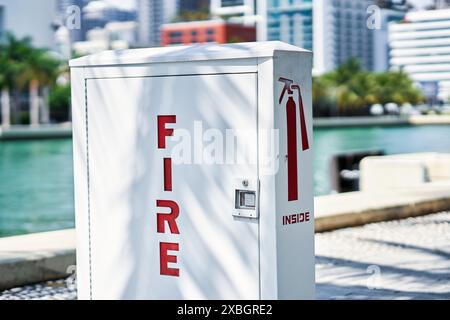 Un estintore rosso e bianco vicino al lungomare di Miami, con un edificio moderno sullo sfondo Foto Stock