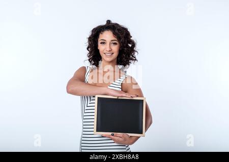 Una giovane donna d'affari, fiduciosa e accogliente, sorridente, ha un cartello con la lavagna con spazio per lo slogan pubblicitario o la messaggistica di concetto chiave. Copia spazio Foto Stock