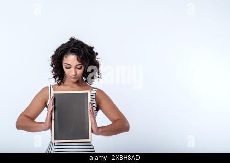 Una giovane donna d'affari, fiduciosa e accogliente, sorridente, ha un cartello con la lavagna con spazio per lo slogan pubblicitario o la messaggistica di concetto chiave. Copia spazio Foto Stock